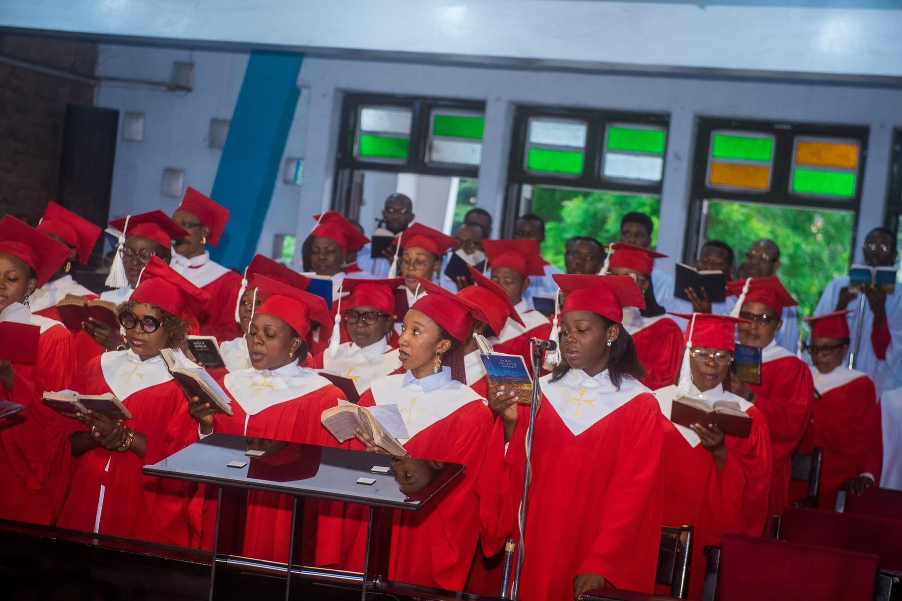 The choir of All Saints’ Cathedral, Onitsha, in red robes with white yokes and red caps, singing from their hymn books at a Sunday service.