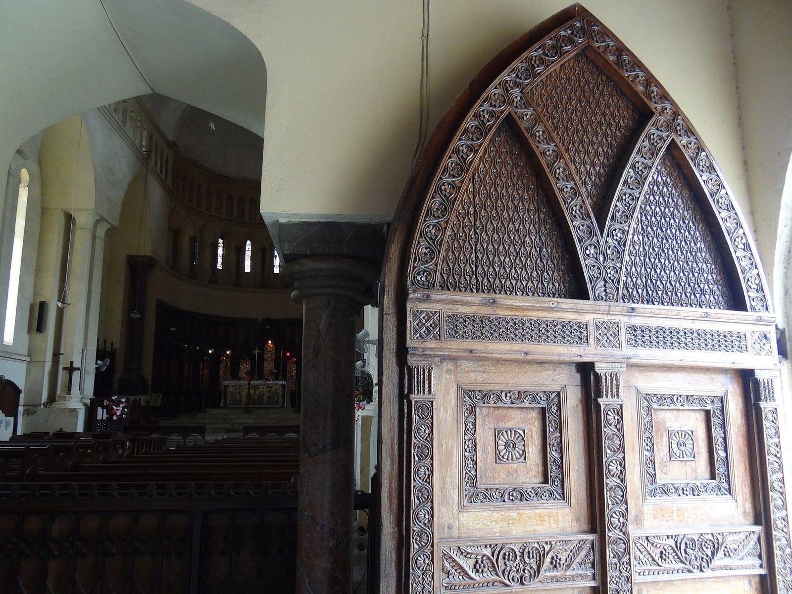 A richly carved Zanzibari wooden door under a pointed arch at Christ Church Cathedral, Stone Town, with the nave visible beyond.